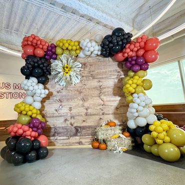 Rustic wooden backdrop with autumn balloon garland, dried florals, hay cubes, corn and pumpkins.