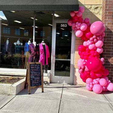 Fluffy pink balloon garland installed outside a clothing store entrance.