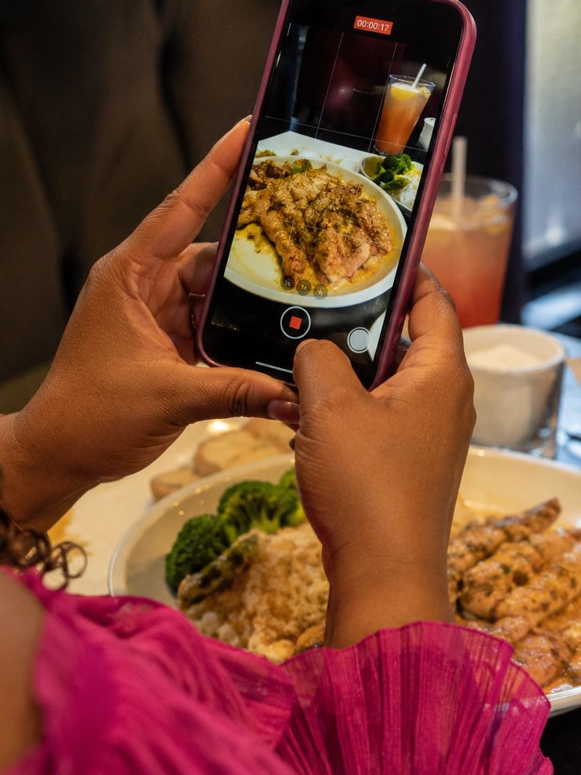 Person recording a plate of grilled chicken with broccoli and rice on their smartphone.