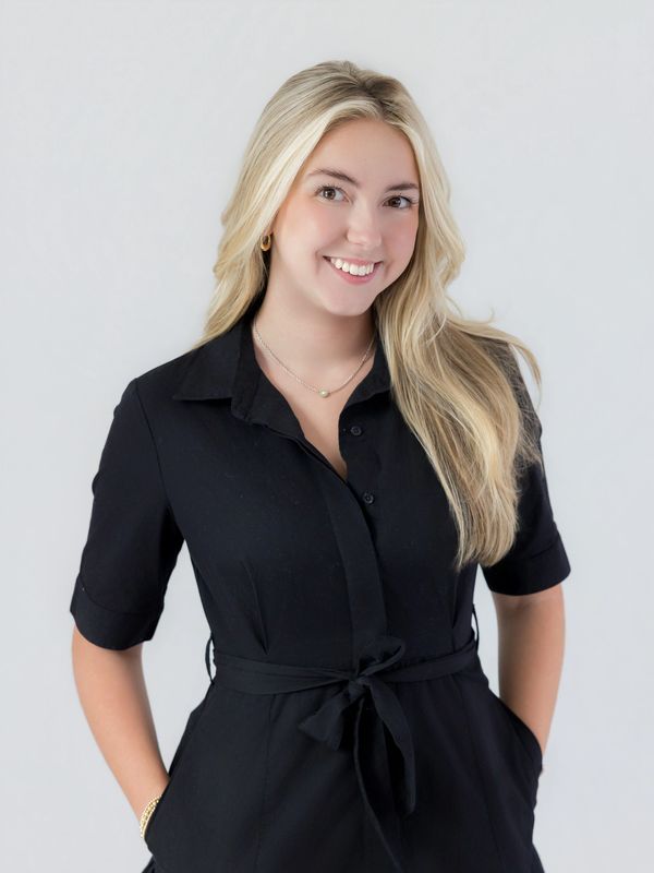 Smiling woman in a black dress with hands in pockets.