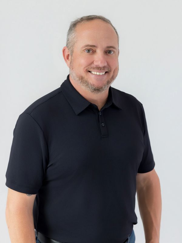 Smiling man in black polo shirt against white background.