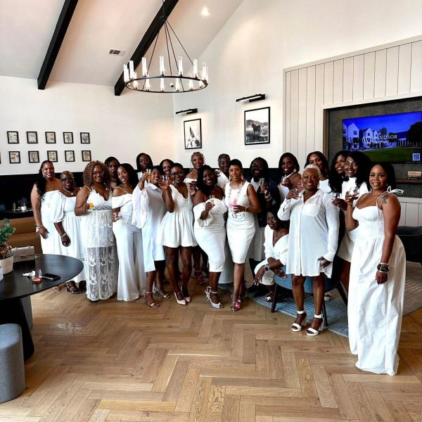 Group of women dressed in white holding drinks, posing indoors.
