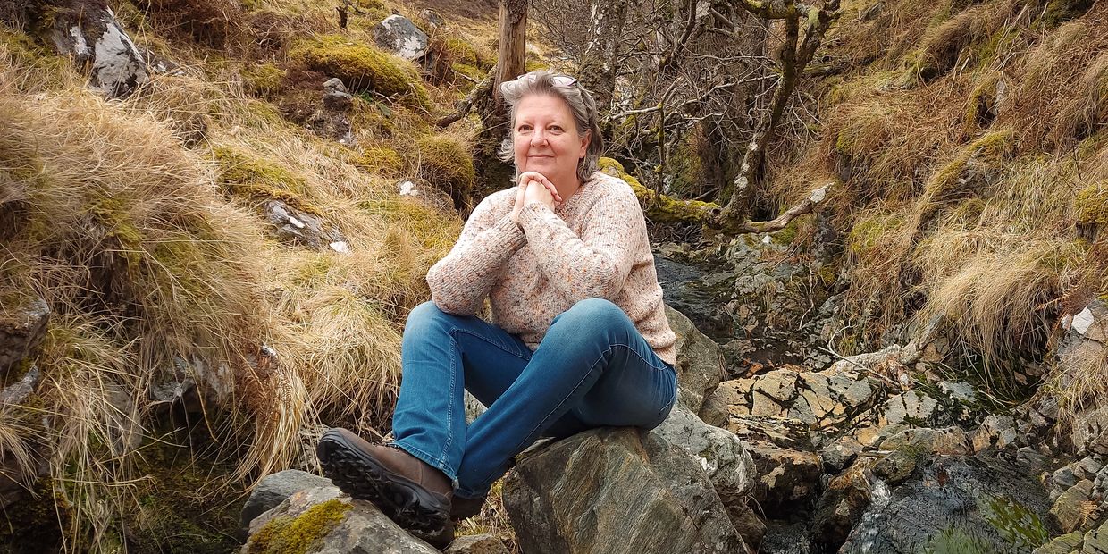 Woman sitting on rocks in a natural, grassy area.