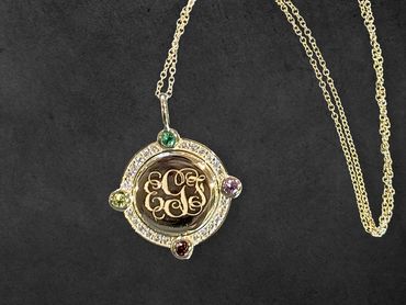 Elegant monogrammed pendant with gemstones on a silver chain.
