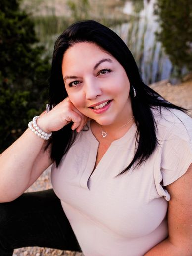 A smiling woman with black hair sitting outdoors near water.