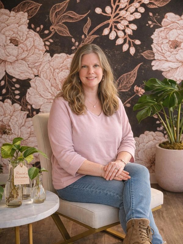 Woman sitting on a chair with a floral backdrop and plants nearby.