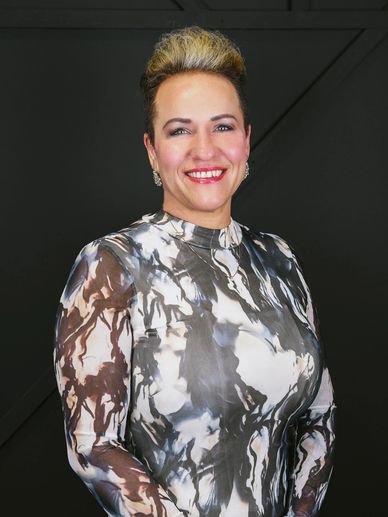 Smiling woman in a stylish black and white patterned dress against a dark background.