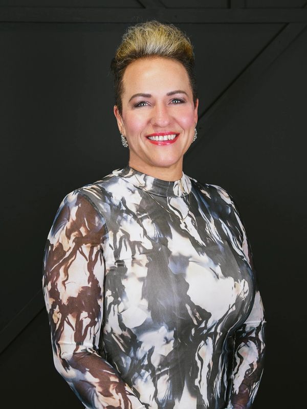 Smiling woman in a stylish black and white patterned dress against a dark background.