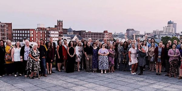 Large group of diverse women standing outdoors with city skyline in background.