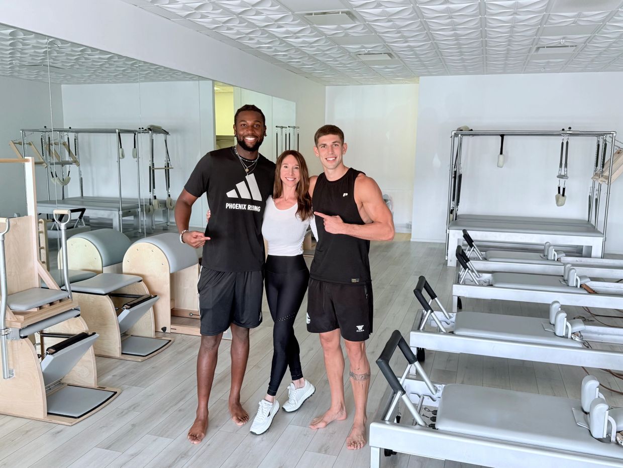 Three people in workout attire in a Pilates studio.