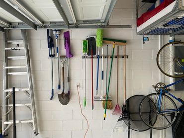 Garage wall with neatly organized garden and cleaning tools hanging on hooks.