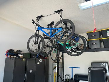 Two bicycles hanging from a ceiling rack in a garage.