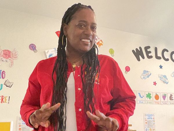 Woman in red jacket smiling and making peace signs indoors.
