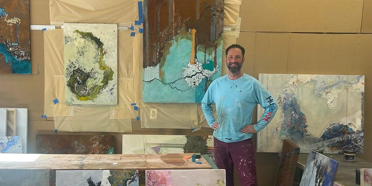 Artist standing confidently in front of his abstract paintings in a studio.