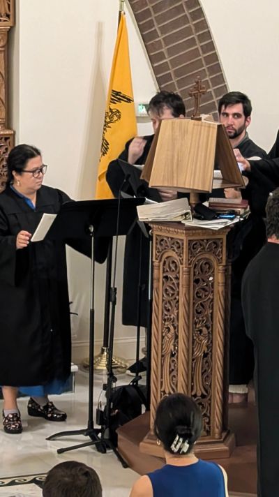 Choir members singing in a church with a yellow flag in the background.