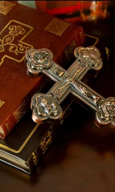 Ornate metal cross resting on intricately designed religious books.