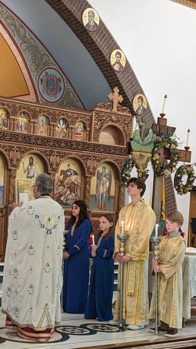 Children and a priest participate in a religious ceremony inside a decorated church.
