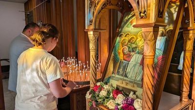 A person lighting a candle in front of a religious icon inside a church.