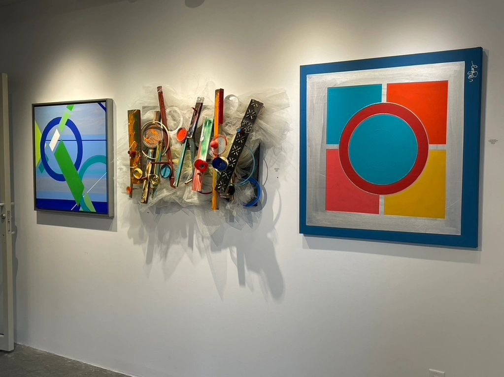 Three colorful abstract artworks displayed on a gallery wall.