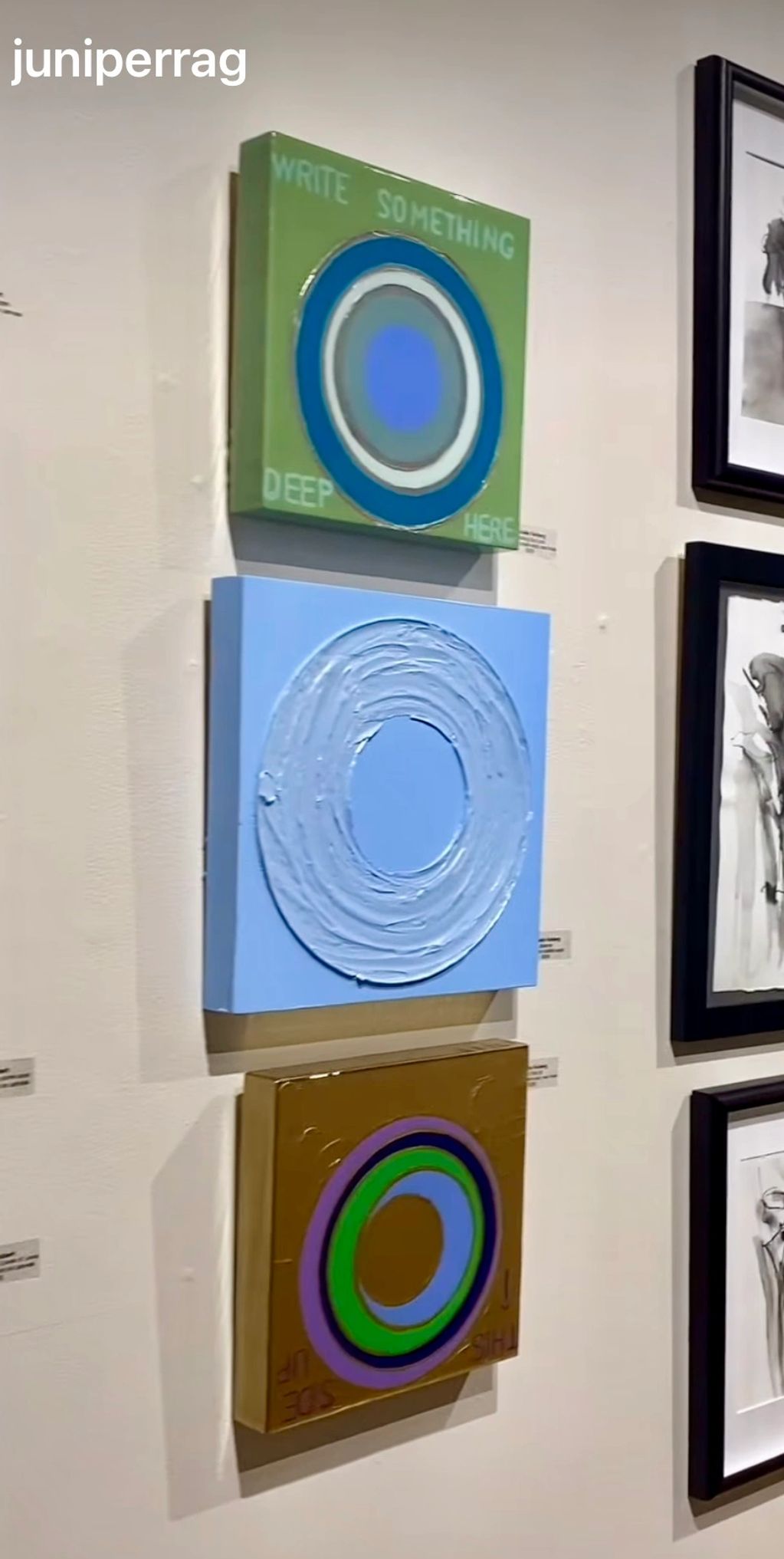 Three colorful circular abstract paintings displayed vertically on a white wall.