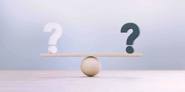Black and white question marks balanced on a wooden seesaw over a round pivot.