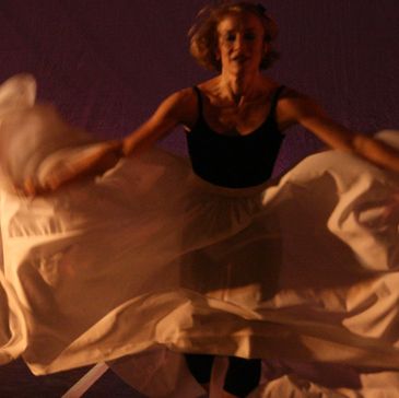 A dancer gracefully moves with flowing fabric in dim light.