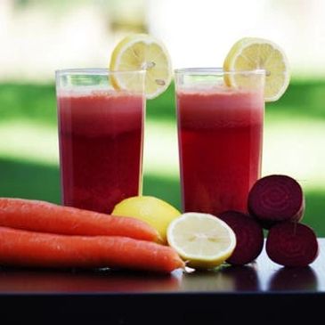 Two glasses of fresh beet and carrot juice with lemon slices on top.