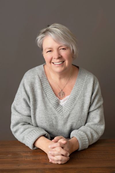 Smiling woman in a cozy gray sweater sits at a wooden table.