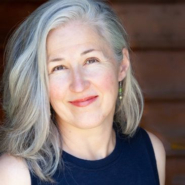 Smiling woman with silver hair in a black sleeveless top.