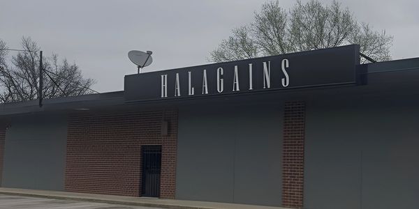 Building with "HALAGAINS" sign and empty parking lot under cloudy sky.