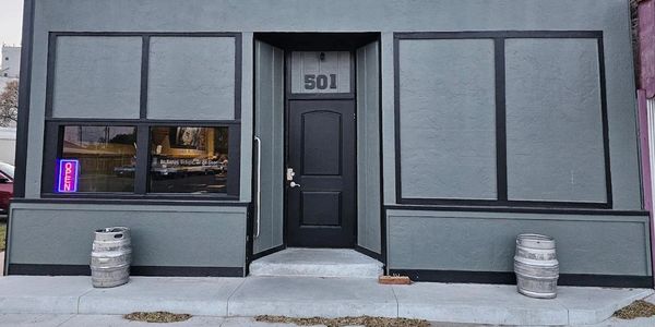 Minimalist storefront with gray walls, black door, and beer kegs.