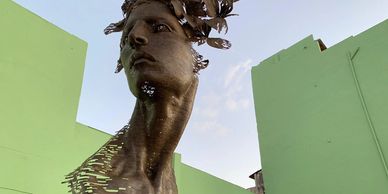 Modern metal sculpture of a woman's head with fragmented design against green walls.