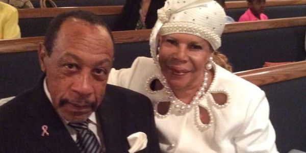 Elegant elderly couple dressed formally, seated in a church pew.