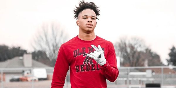 Young athlete in red Ole Miss Rebels shirt holding football on field.
