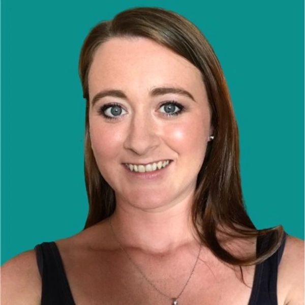 Image of me in front of a plain, teal coloured background. My hair is down and I'm smiling