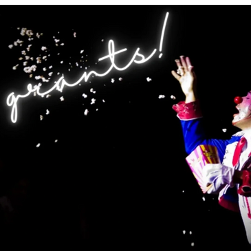 A clown blowing the word "grants" into a black sky