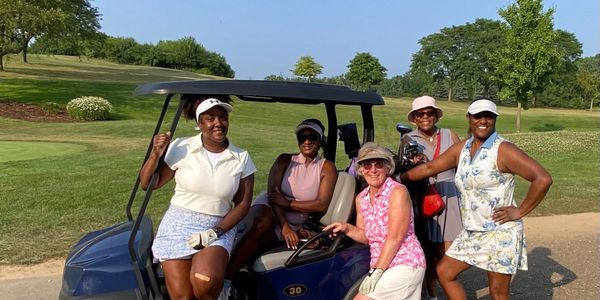 Five women golfers posing with a golf cart on a sunny day.