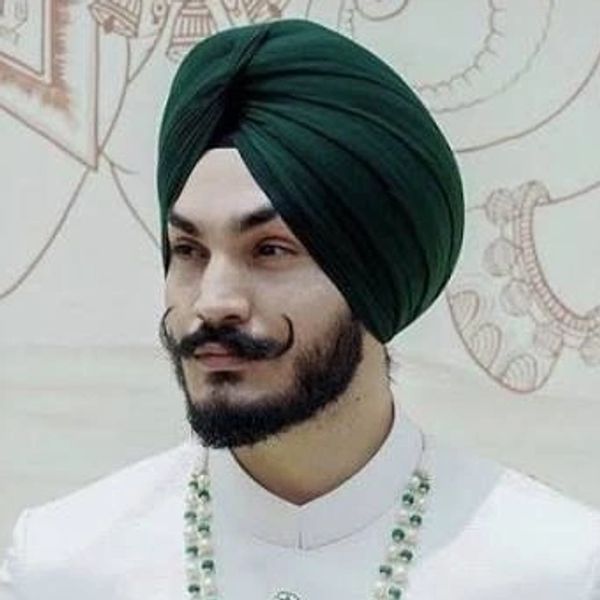 Man in traditional white attire and green turban with a decorative necklace.