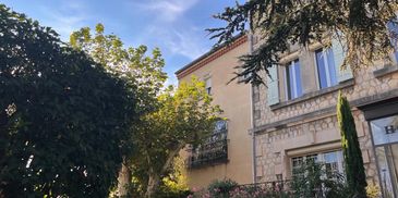 Stone building with windows surrounded by trees and bushes under a blue sky.