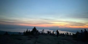 Silhouetted people watching a colorful sunset over a rocky landscape.
