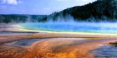 Colorful geothermal pool with steam and surrounding forested hills.