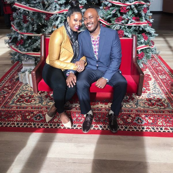 A couple sitting on a red bench in front of Christmas trees, smiling and holding hands.