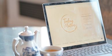 Laptop displaying a website with 'Today Matters' message, beside tea set.