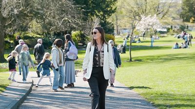 Woman walking confidently in a sunny park with people enjoying the day around her.