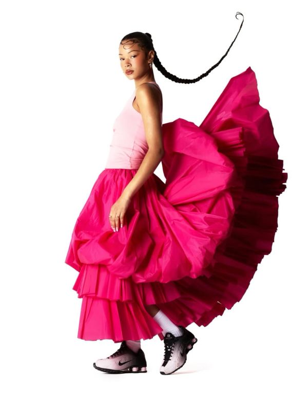 Woman in vibrant pink skirt and sneakers with braided hair flying.