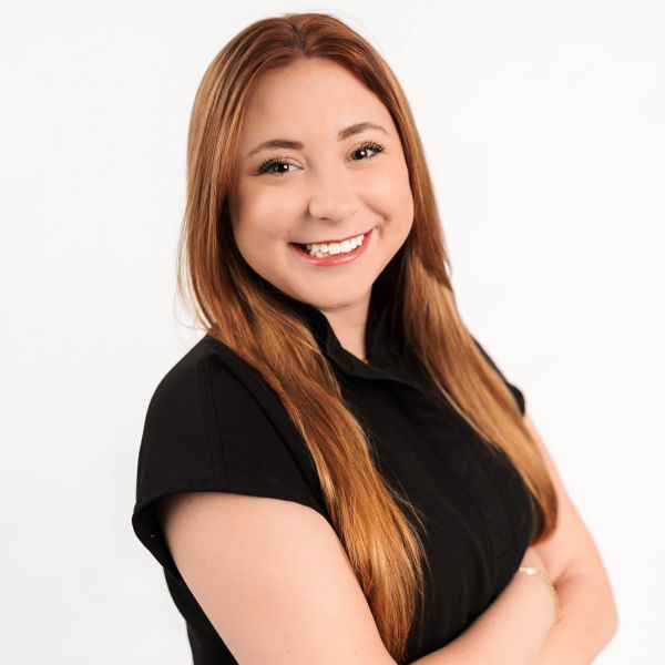Smiling woman with long red hair in black top posing confidently.