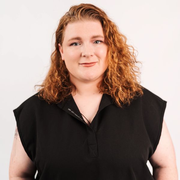 Confident woman with curly red hair wearing a black top, smiling gently at the camera.