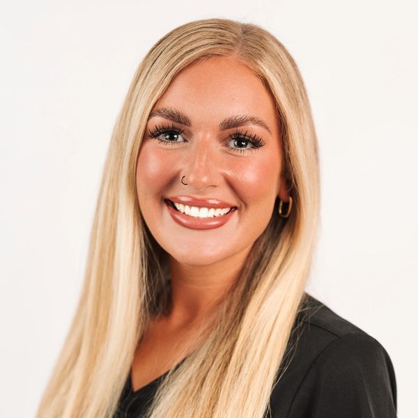 Smiling blonde woman with long hair and a nose ring against a white background.