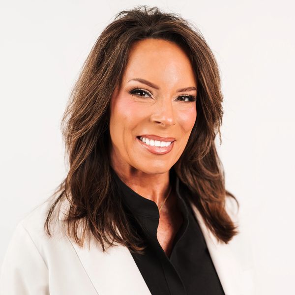 Professional woman with brown hair smiling in a white blazer.