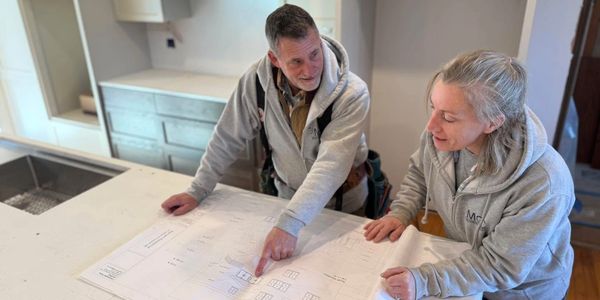 Two people reviewing architectural plans in a kitchen under renovation.